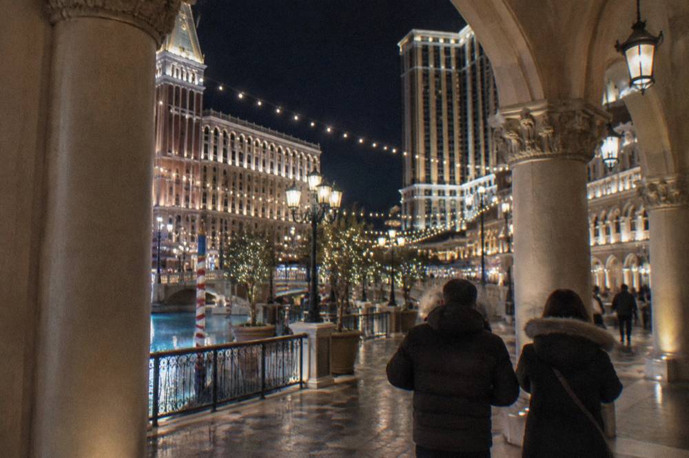 A resort promenade at night with holiday lighting strung above the walkway