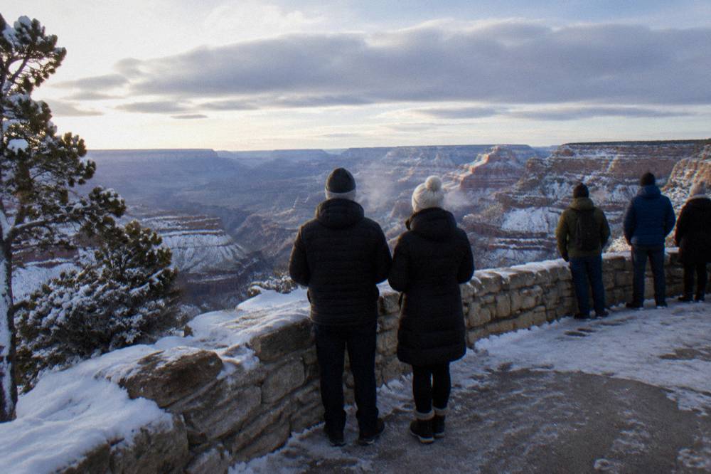 Winter visitors in winter coats standing at a snowy South Rim overlook