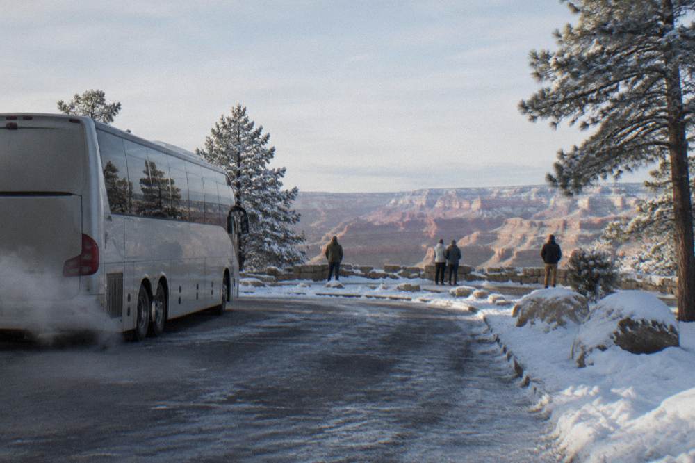 A tour bus parked at a Grand Canyon overlook with snow patches on the ground