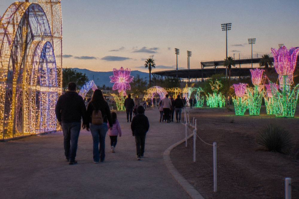 A lit walkway winding through a large outdoor Christmas light maze with families strolling between illuminated displays.