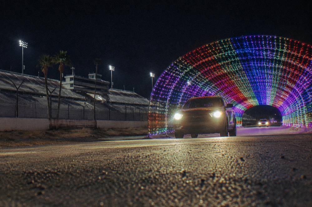 A car driving through a tunnel of colored holiday lights at night