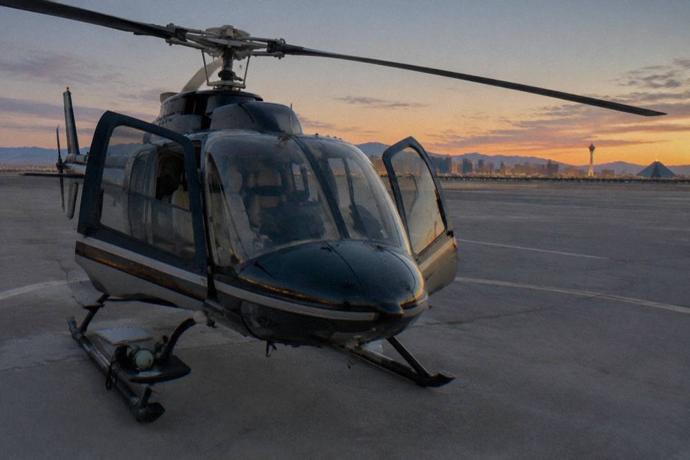 A helicopter on a lit heliport pad at dusk with the Strip skyline in the distance