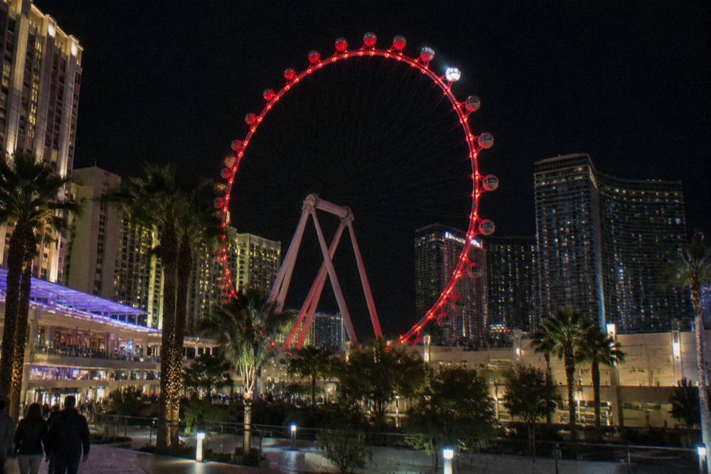 An observation wheel cabin glowing red beside resort towers after dark