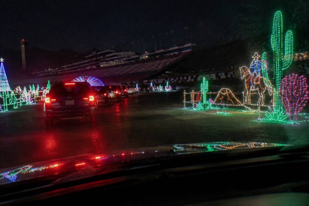 A long line of colorful holiday light displays stretching along a drive-through course at night