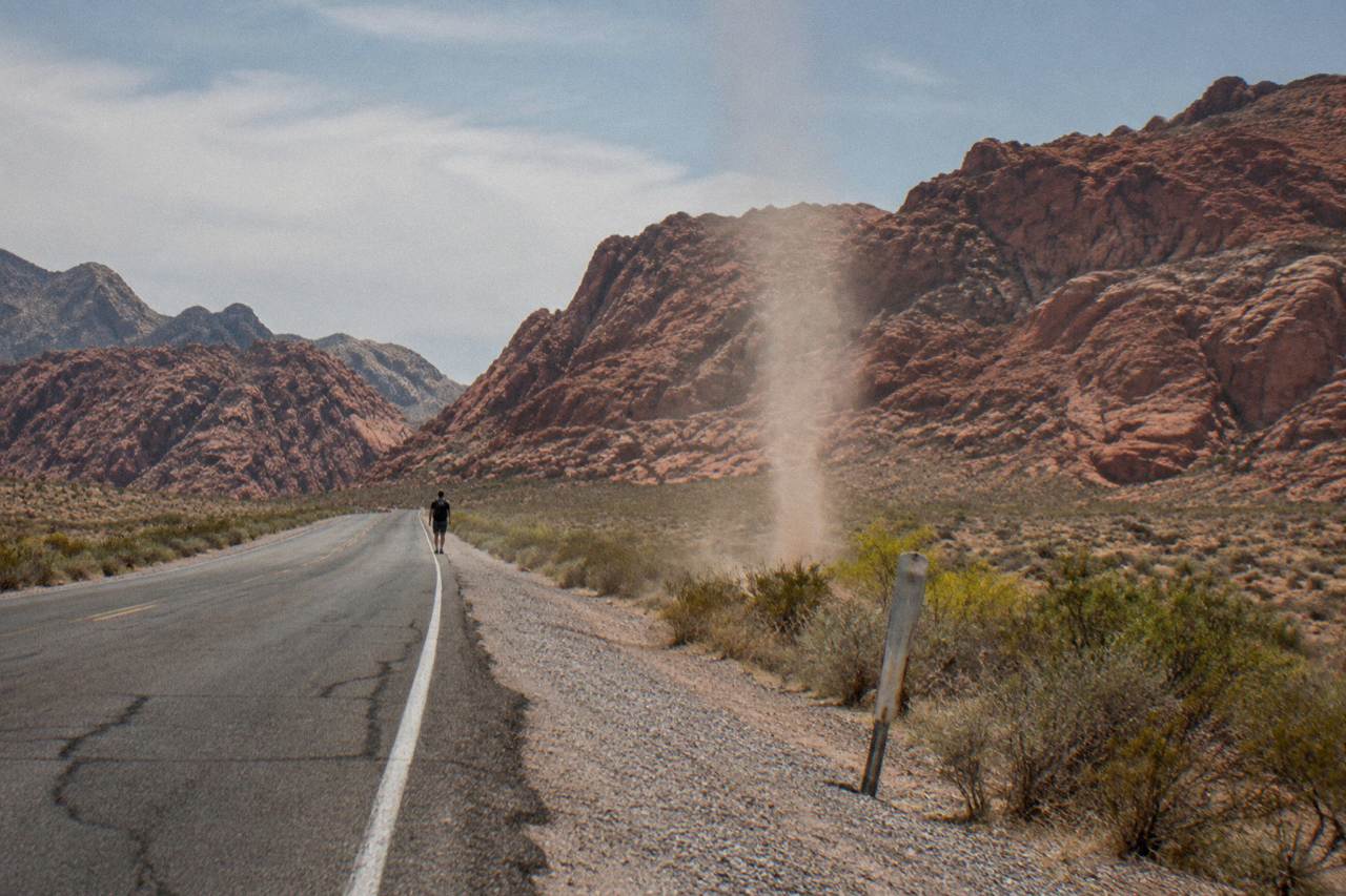 Desert highway stretching toward red rock cliffs under a wide afternoon sky