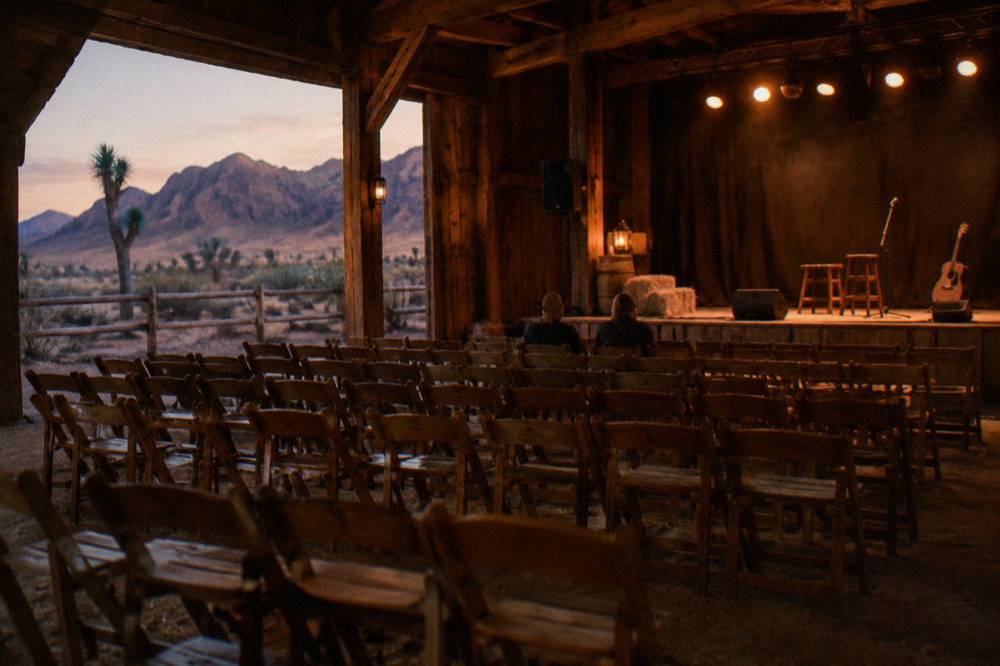 A rustic wooden barn interior set for a dinner show with stage lighting and empty chairs