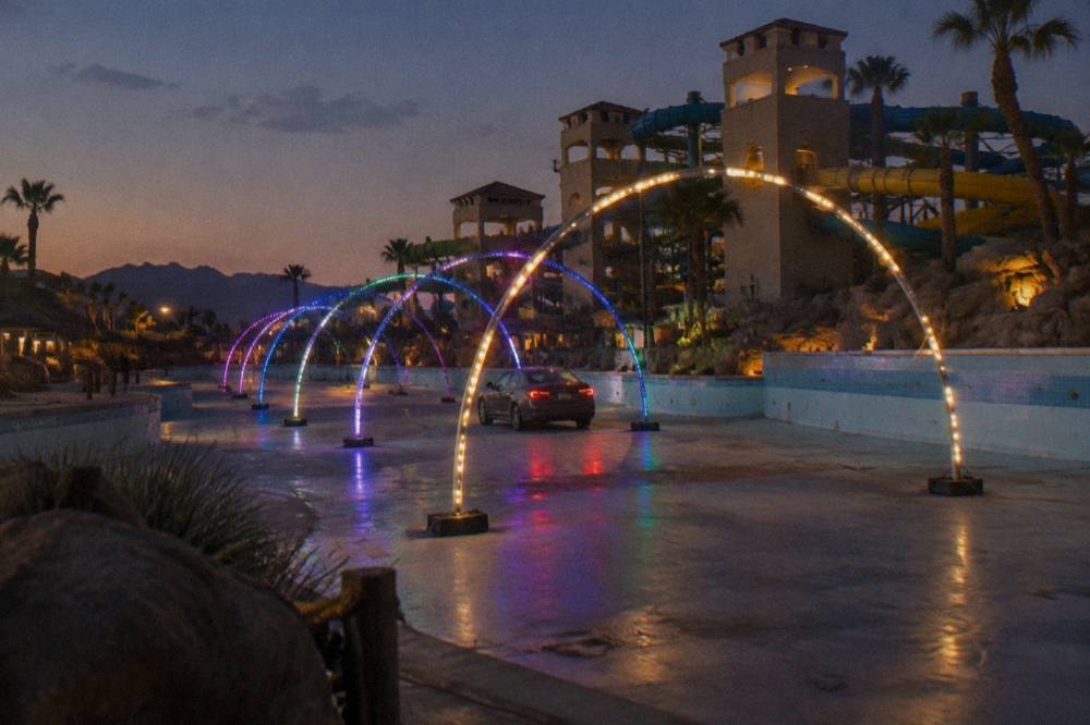 A car winding through glowing holiday light arches on a dark speedway course