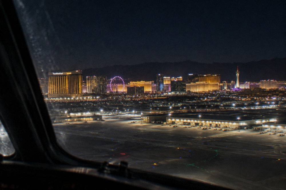 A helicopter cockpit view of the Las Vegas Strip glowing at night with the High Roller wheel visible