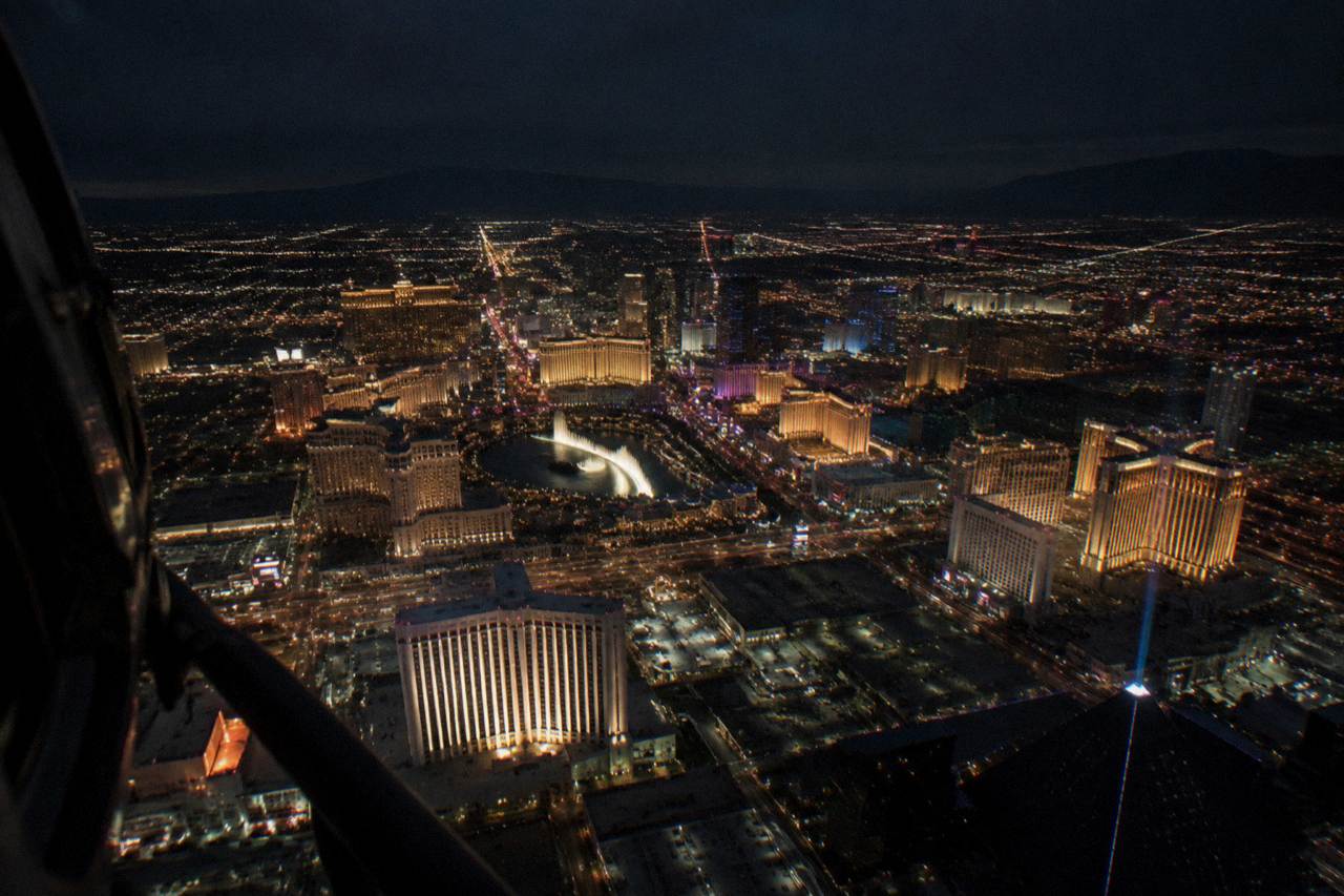 A helicopter flying over the illuminated Las Vegas Strip at night with resort towers lit below
