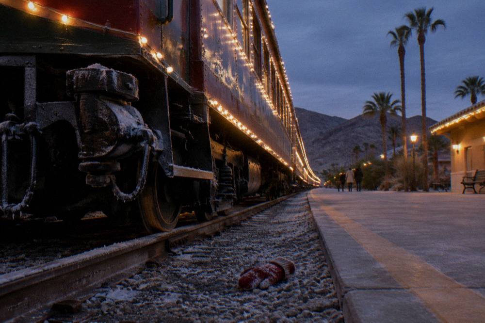 A vintage passenger train decorated with warm white lights waiting at a station platform after dark