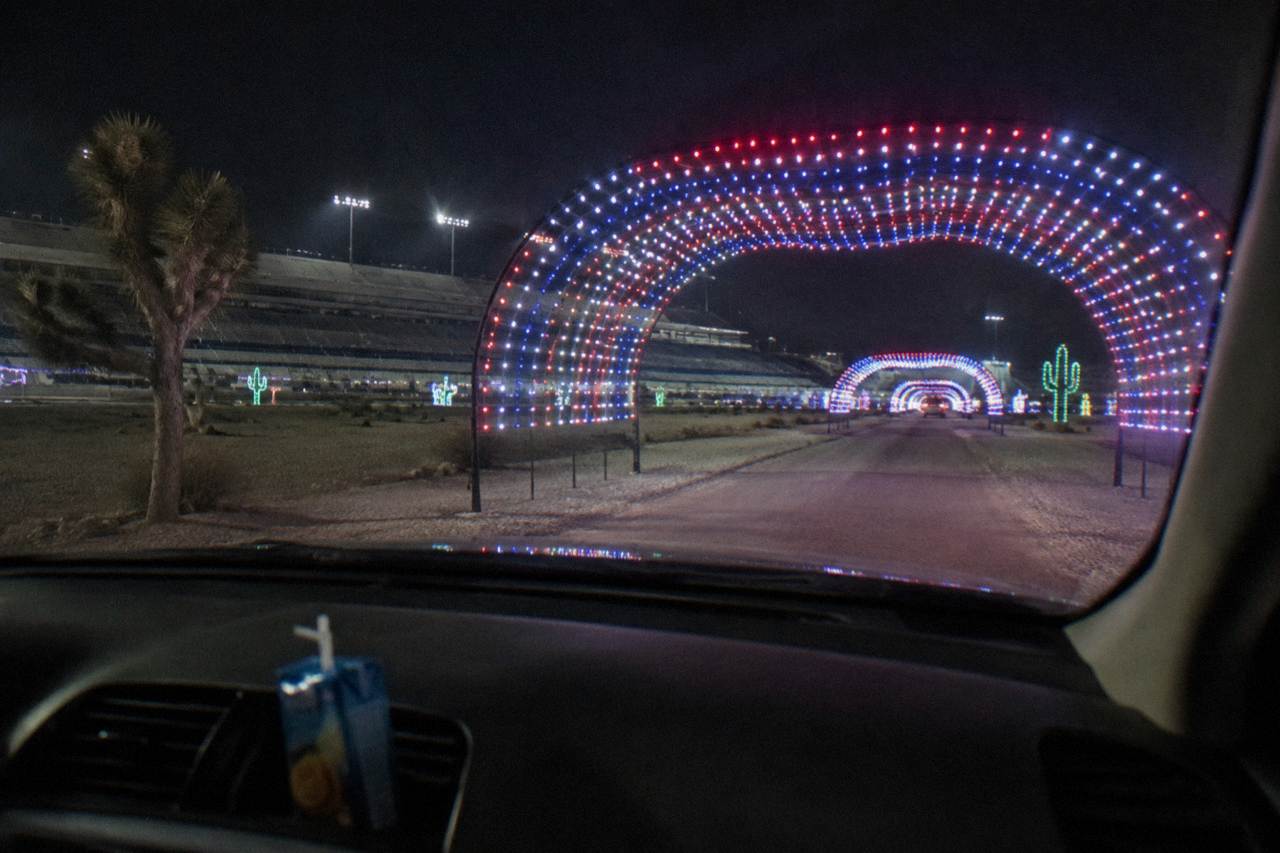 A holiday light display with glowing tunnels and colorful illuminated trees along a drive-through course at night