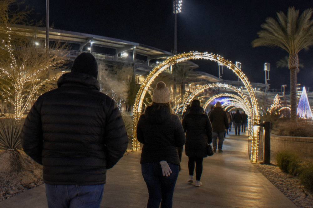 Warmly dressed visitors walking between glowing light archways on an outdoor path at night