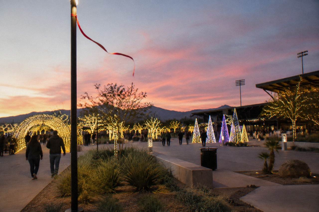 Festive light displays glowing across an outdoor ballpark plaza at dusk