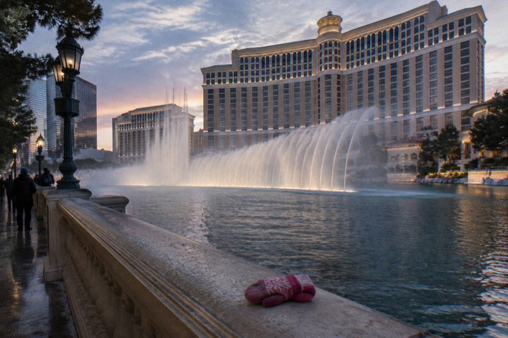 Water jets rising from a lake in front of a lit hotel tower at dusk