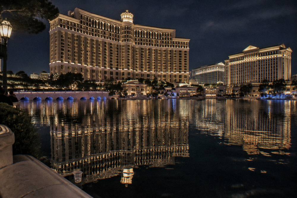 A lit hotel tower and promenade reflected in a lake at night