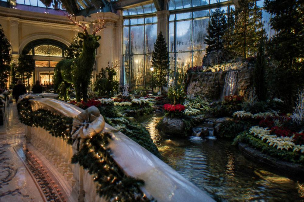 Ornamental bridges and seasonal topiary lit by warm light inside a glass garden hall