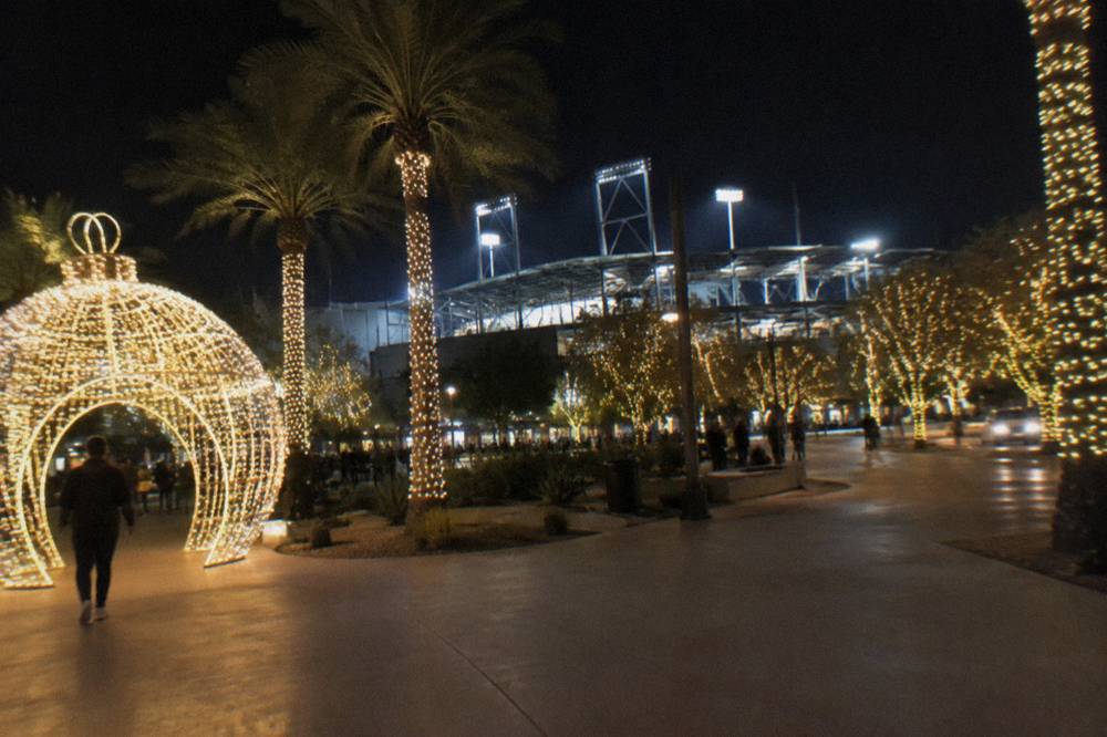 A ballpark plaza at night with holiday light installations and glowing trees