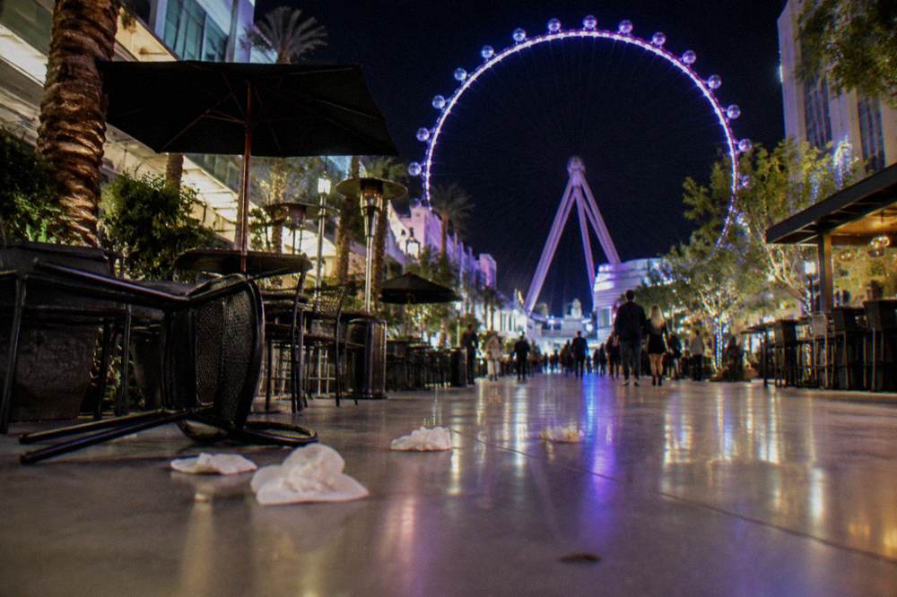 A lit pedestrian promenade along the Strip at night with glowing signs
