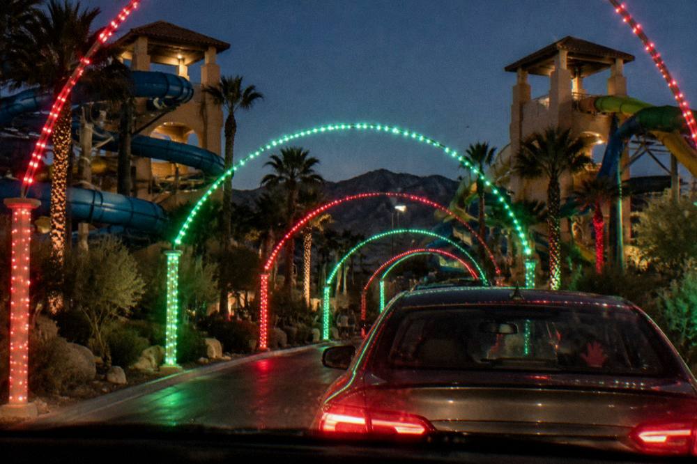 A vehicle driving through a tunnel of colorful holiday lights at night
