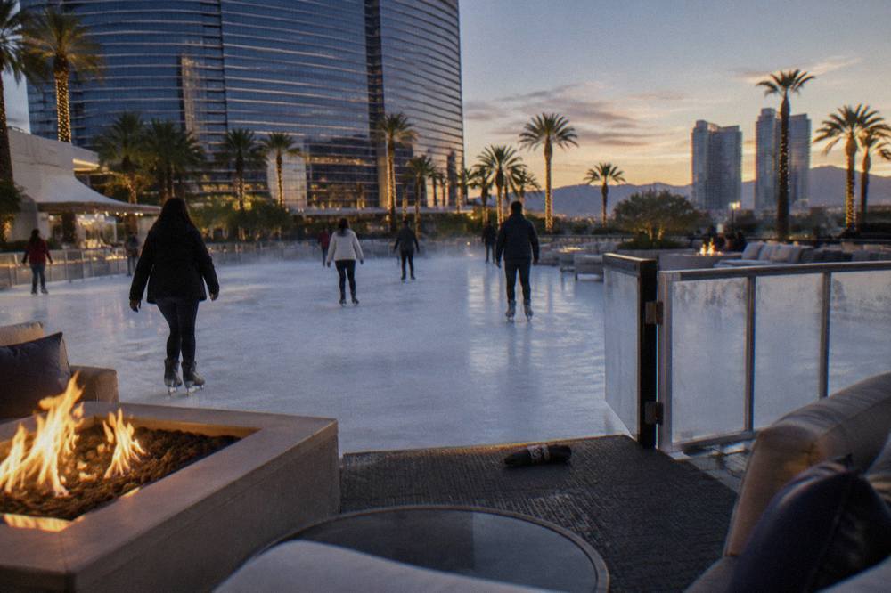 Skaters circling an outdoor rink beside fire pits and lounge seating