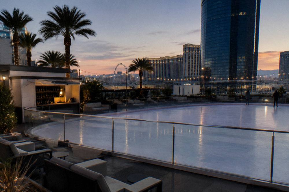A quiet ice rink at dusk with empty lounge chairs and lit string lights
