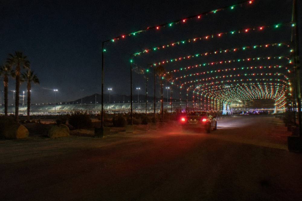 A vehicle driving through a tunnel of holiday lights on a speedway course at night