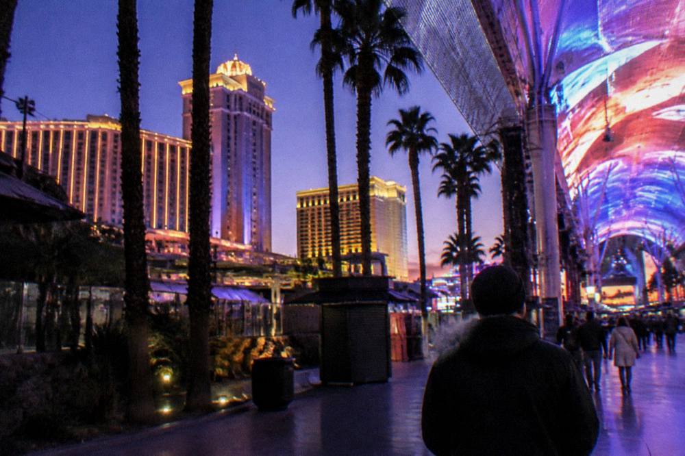 A Las Vegas street at dusk with palm trees and lit resort towers under a cold clear sky