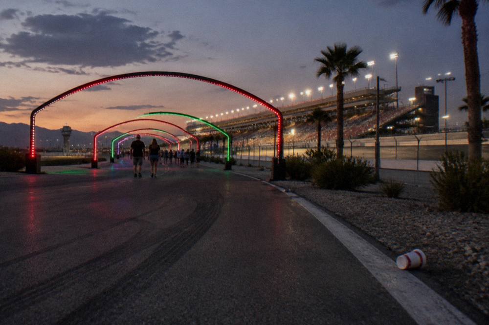 A long driveway lined with glowing holiday light arches leading toward a lit grandstand