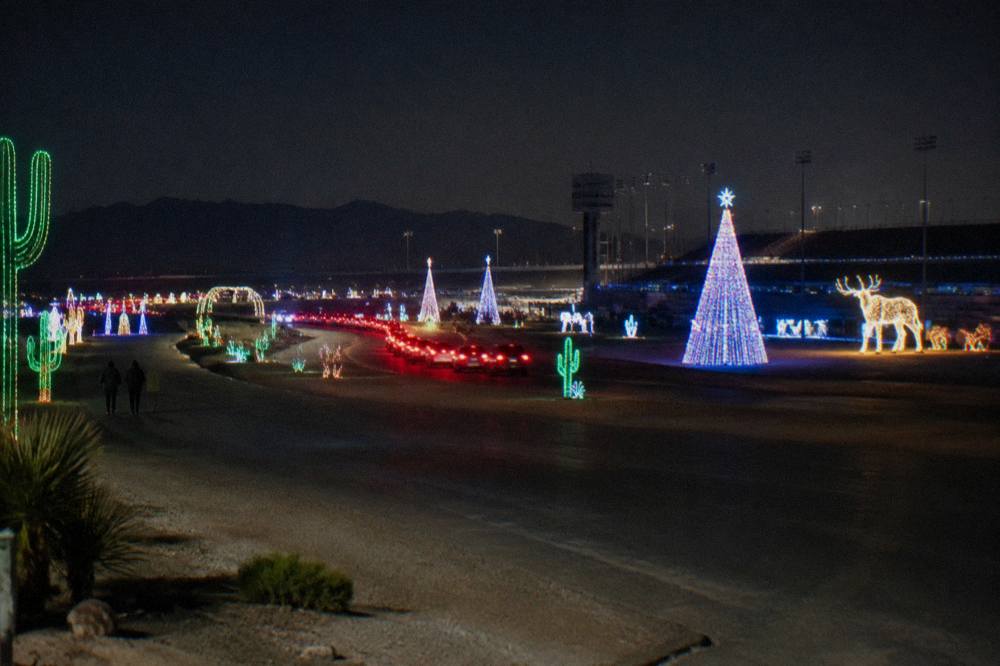 A long line of red taillights snaking through a field of illuminated holiday displays at night
