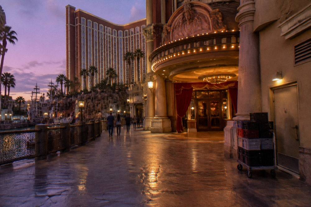 A grand theater exterior with illuminated signage along a resort promenade at dusk