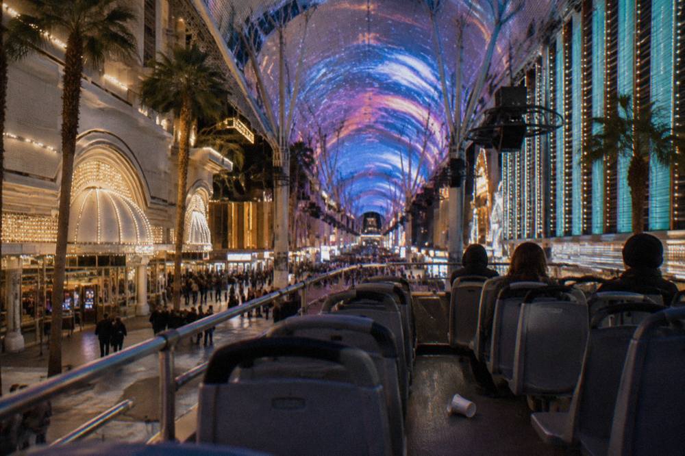 Upper deck of an open-top tour bus at night with the glowing lights of resort towers rising on both sides of the street