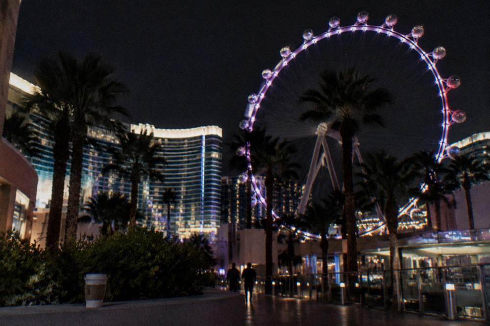 A large observation wheel beside the Strip at night with the wheel's cabins lit and resort towers behind it
