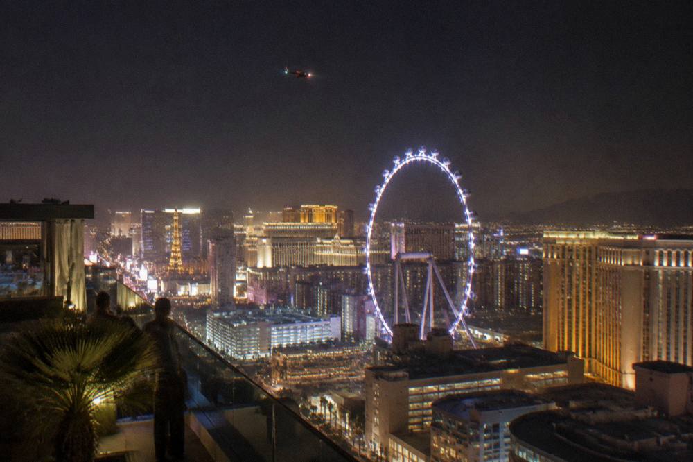 A helicopter flying at night above a brightly lit resort boulevard with the city glowing below