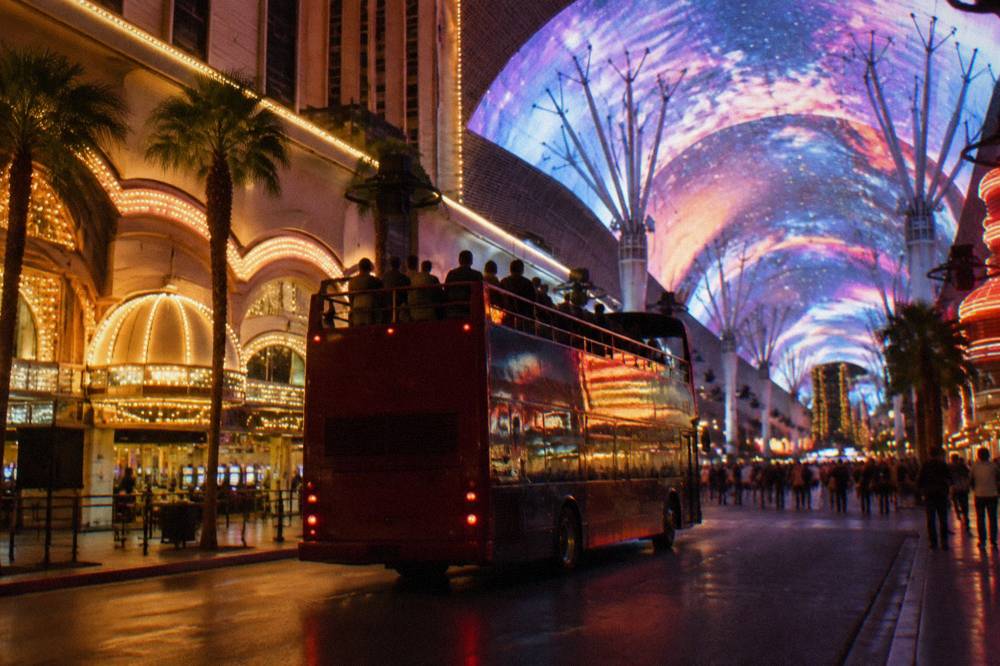 An open-top double decker bus on a Las Vegas street at night with illuminated buildings around it