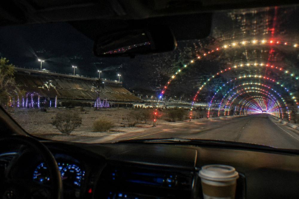 A car driving through a tunnel of holiday lights at a drive-through display