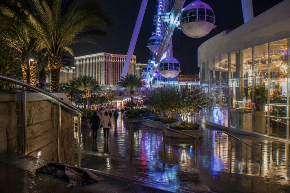 An illuminated observation wheel rising above a lit promenade at night