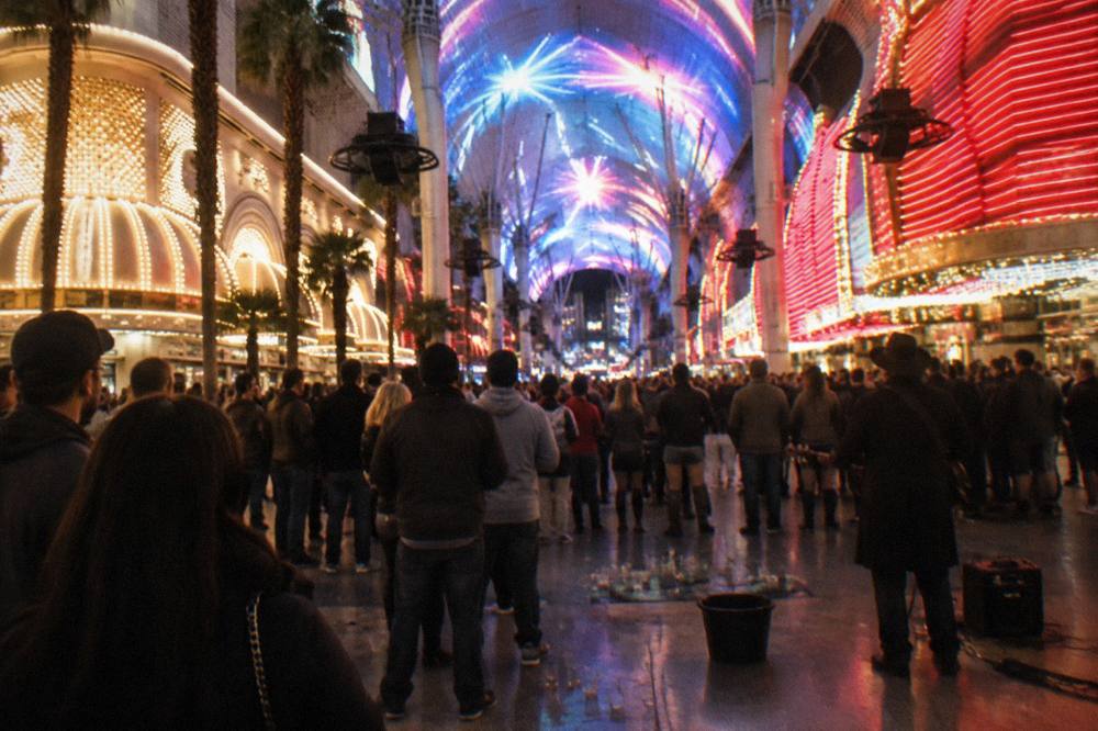 Crowds gathered along a lit city street at night with glowing signage overhead