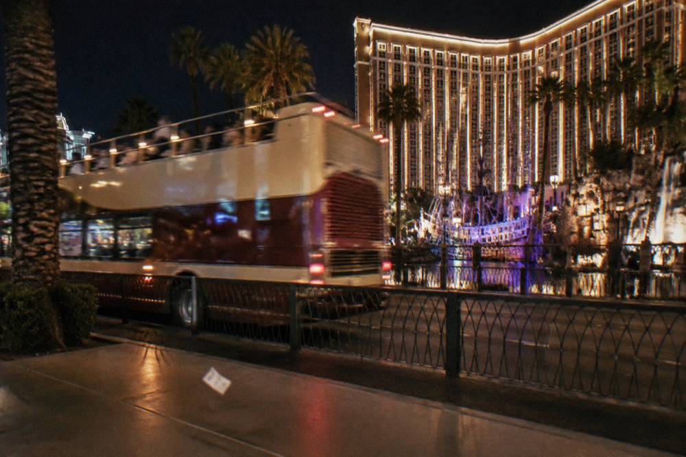 Open-top sightseeing bus driving along the illuminated Las Vegas Strip at night