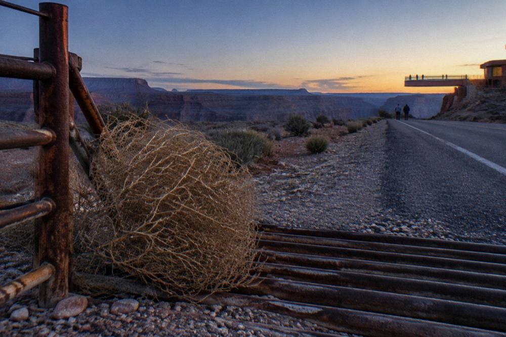 An open desert road at dusk with distant canyon mesas on the horizon