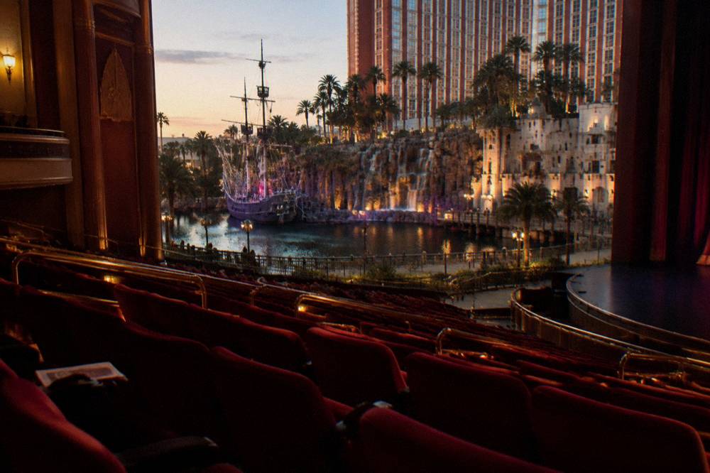 A grand theater interior with red seating and a lit stage before an evening performance
